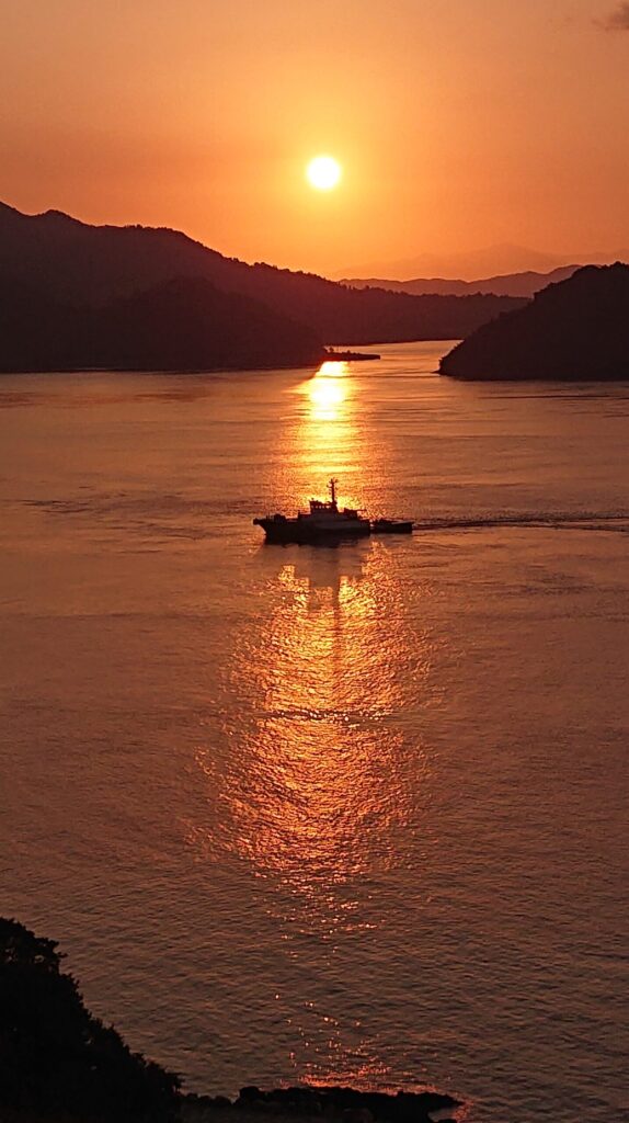 海面に伸びる朝日のラインと交差する船体