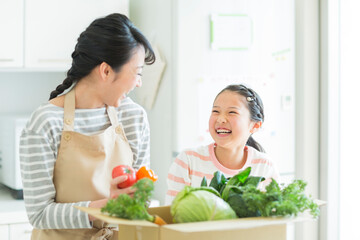 野菜の入った箱を持って母娘が微笑み合っている画像